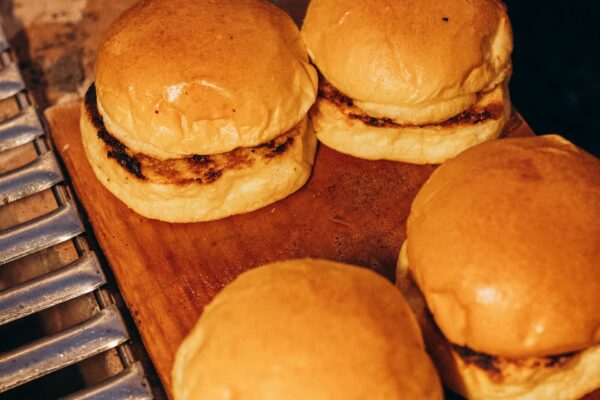 Sultingas triušienos mėsainis su šviežiomis daržovėmis ir padažu ant medinio pagrindo.