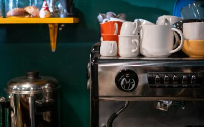 Modernus kavos aparatas stovi jaukioje namų virtuvėje šalia garuojančio kavos puodelio.