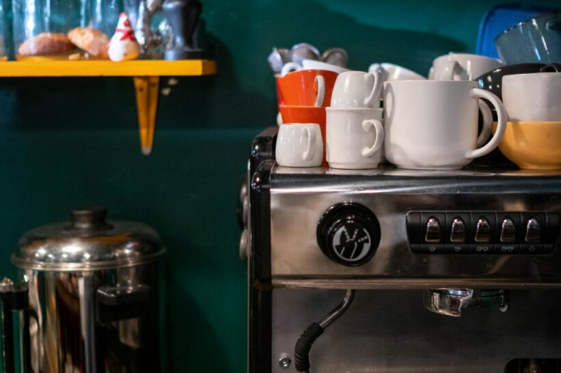 Modernus kavos aparatas stovi jaukioje namų virtuvėje šalia garuojančio kavos puodelio.